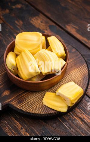 Süße, goldene Jackfrucht-Schoten (Zwiebeln) in einer Holzschale auf einem rustikalen dunklen Holztisch. Tropischer Obstsnack mit Kopierbereich Stockfoto