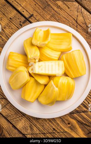 Süße, goldgelbe Jackfruchskapseln (Zwiebeln), serviert auf einem weißen Teller auf einem rustikalen Holztisch. Frischer, tropischer Obstsnack Stockfoto