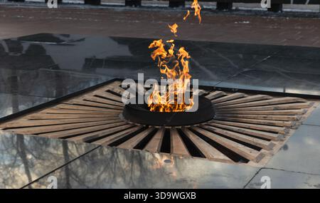 Eine symbolische Gedenkstätte für ewige Flammen in einer kreisförmigen Struktur mit reflektierenden Oberflächen und einem lebendigen Feuer, das Erinnerung und Ehre repräsentiert Stockfoto