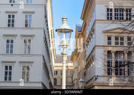 Klassische Straßenlaterne auf der Wiener Straße mit kunstvollen Gebäuden und klarem blauem Himmel. Reise-, Architektur- und urbanes Lifestyle-Thema. Stockfoto