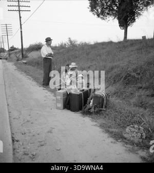 Dieses Foto dokumentiert eine trampende Familie, die während der Großen Depression auf einer Autobahn in Macon, Georgia, wartet. Der Vater ist ein Reparaturmann, der Nähmaschinen, Rasenmäher und andere kleine Geräte repariert, aber er ist gezwungen, Macon zu verlassen, weil die Stadt eine Lizenzgebühr von 25 US-Dollar benötigte – ein Betrag, den er sich nicht leisten konnte. Die Reise der Familie zurück nach Alabama spiegelt die weit verbreitete wirtschaftliche Vertreibung, Mobilität und Überlebensstrategien der Arbeiterfamilien in den 1930er Jahren wider und hebt die Barrieren hervor, denen sich informelle Arbeiter und kleine Handwerker gegenübersehen. Stockfoto