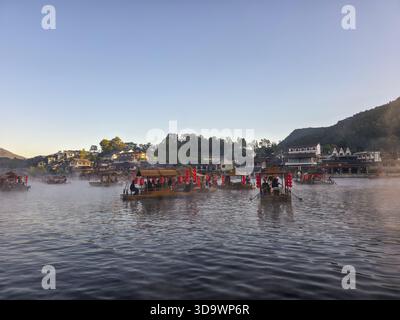 Ruhige Morgenlandschaft mit nebeligem Fluss und traditioneller Bambus-Floß-Tour. Friedliche Reiseszene mit einem Dorf am Fuße des Berges, das eine ruhige V Stockfoto