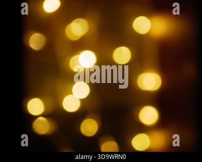 Warme goldene Bokeh-Lichter, die sanft vor dunklem Hintergrund leuchten, abstrakte Weihnachtsstimmung, defokussierte Feenlichter-Textur. Pro Foto. Hoch Stockfoto