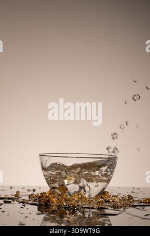 Die mit Wasser gefüllte Schüssel steht auf einer Ebenen Oberfläche. Seifenblasen platzen auf und erzeugen Spritzer, die Tropfen in die Luft schicken, um eine verspielte Szene zu präsentieren. Die Einstellung ist einfach und in Innenräumen. Stockfoto