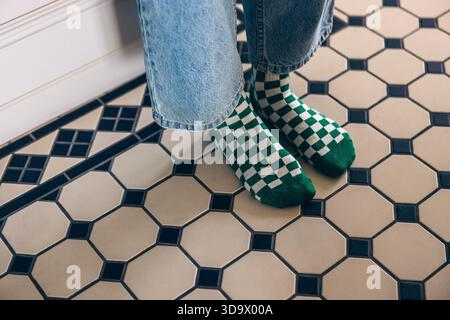 Person mit grün-weiß karierten Socken und Jeans, die auf einem gemusterten Fliesenboden steht und eine gemütliche und stilvolle Innenatmosphäre schafft Stockfoto