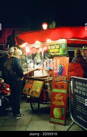 Bath, England - 3. Dezember 2025: Bath Christmas Market, mit Verkaufsständen, Verkaufsständen und Käufern. Aufgenommen nach Einbruch der Dunkelheit auf Spezialfilm. Stockfoto