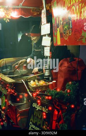 Bath, England - 3. Dezember 2025: Bath Christmas Market, mit Verkaufsständen, Verkaufsständen und Käufern. Aufgenommen nach Einbruch der Dunkelheit auf Spezialfilm. Stockfoto