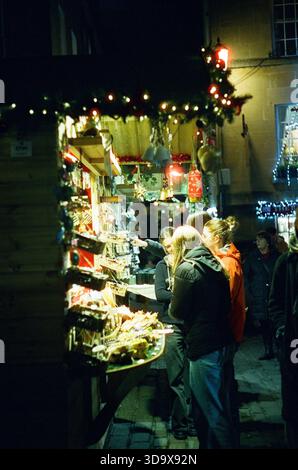 Bath, England - 3. Dezember 2025: Bath Christmas Market, mit Verkaufsständen, Verkaufsständen und Käufern. Aufgenommen nach Einbruch der Dunkelheit auf Spezialfilm. Stockfoto