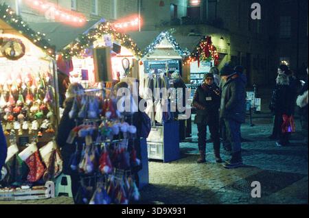 Bath, England - 3. Dezember 2025: Bath Christmas Market, mit Verkaufsständen, Verkaufsständen und Käufern. Aufgenommen nach Einbruch der Dunkelheit auf Spezialfilm. Stockfoto