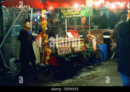 Bath, England - 3. Dezember 2025: Bath Christmas Market, mit Verkaufsständen, Verkaufsständen und Käufern. Aufgenommen nach Einbruch der Dunkelheit auf Spezialfilm. Stockfoto