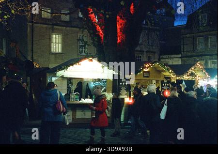 Bath, England - 3. Dezember 2025: Bath Christmas Market, mit Verkaufsständen, Verkaufsständen und Käufern. Aufgenommen nach Einbruch der Dunkelheit auf Spezialfilm. Stockfoto
