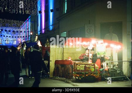 Bath, England - 3. Dezember 2025: Bath Christmas Market, mit Verkaufsständen, Verkaufsständen und Käufern. Aufgenommen nach Einbruch der Dunkelheit auf Spezialfilm. Stockfoto