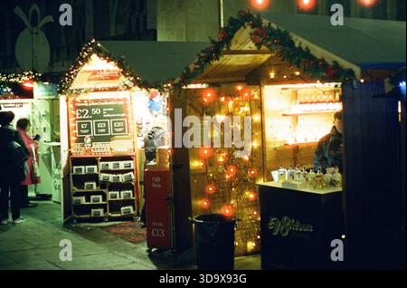 Bath, England - 3. Dezember 2025: Bath Christmas Market, mit Verkaufsständen, Verkaufsständen und Käufern. Aufgenommen nach Einbruch der Dunkelheit auf Spezialfilm. Stockfoto