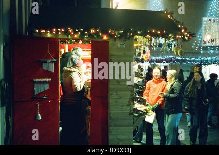 Bath, England - 3. Dezember 2025: Bath Christmas Market, mit Verkaufsständen, Verkaufsständen und Käufern. Aufgenommen nach Einbruch der Dunkelheit auf Spezialfilm. Stockfoto