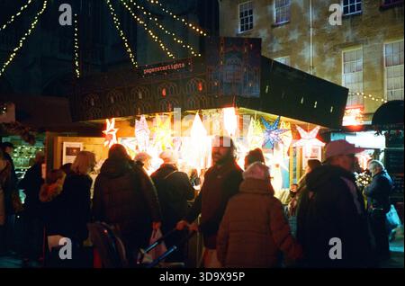 Bath, England - 3. Dezember 2025: Bath Christmas Market, mit Verkaufsständen, Verkaufsständen und Käufern. Aufgenommen nach Einbruch der Dunkelheit auf Spezialfilm. Stockfoto