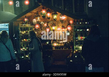 Bath, England - 3. Dezember 2025: Bath Christmas Market, mit Verkaufsständen, Verkaufsständen und Käufern. Aufgenommen nach Einbruch der Dunkelheit auf Spezialfilm. Stockfoto