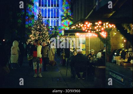 Bath, England - 3. Dezember 2025: Bath Christmas Market, mit Verkaufsständen, Verkaufsständen und Käufern. Aufgenommen nach Einbruch der Dunkelheit auf Spezialfilm. Stockfoto