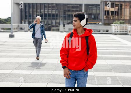 Asiatischer Mann mit rotem Kapuzenpullover und Musik auf dem Dach mit Kopfhörern, Rucksack, Kopierraum Stockfoto