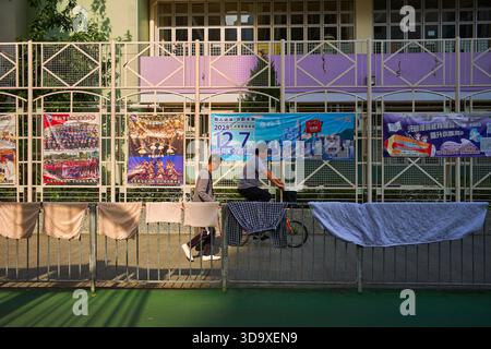 Hongkong, China. Dezember 2025. Ein Mann läuft vorbei und der andere fährt mit dem Fahrrad an einer Schule vorbei, in der sich ein Wahllokal in Tin Shui Wai befindet. Die Parlamentswahlen 2025 in Hongkong finden am 7. Dezember 2025 statt, um die 90 Mitglieder des 8. Hongkonger Legislativrates zu wählen. Quelle: SOPA Images Limited/Alamy Live News Stockfoto