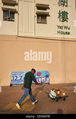 Hongkong, China. Dezember 2025. Ein Liefermann kommt an einem Poster vorbei, auf dem die Leute dazu drängen, in Tin Shui Wai zu wählen. Die Parlamentswahlen 2025 in Hongkong finden am 7. Dezember 2025 statt, um die 90 Mitglieder des 8. Hongkonger Legislativrates zu wählen. Quelle: SOPA Images Limited/Alamy Live News Stockfoto