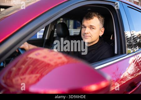 Selbstbewusster Mann, der in rotem Auto sitzt Stockfoto