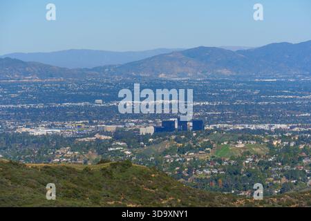 Das Stadtbild von Calabasas erstreckt sich über ein üppiges Tal mit Wohnhäusern, modernen Gebäuden, grünen Hügeln und entfernten, nebeligen Bergen unter einem klaren Himmel Stockfoto