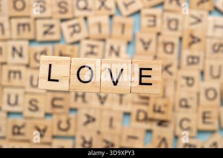 Das Wort „Liebe“ ist mit hölzernen Buchstabenfliesen angeordnet, umgeben von verstreuten Alphabetstücken, wodurch eine warme und ausdrucksstarke Komposition entsteht, die auf Schreibweise fokussiert ist Stockfoto