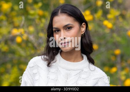 Hispanische Frau posiert zwischen Zitronen im Zitronengarten und trägt weiße Strickpullover goldene Creolen Stockfoto