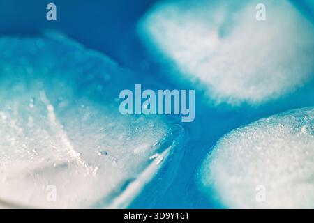 Eine Nahaufnahme von Eiswürfeln in einer blauen Flüssigkeit. Die Eiswürfel sind in der Flüssigkeit verstreut, wodurch ein Gefühl von Bewegung und Fließfähigkeit entsteht. Die blaue Farbe Stockfoto