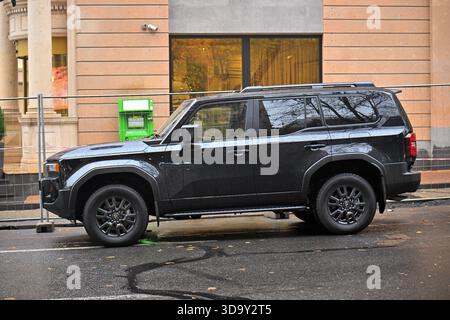 Jerewan Armenien 12.7,2025. Ein schwarzer Geländewagen parkt auf einer nassen Straße. Das Auto steht vor einer grünen Parkuhr Stockfoto