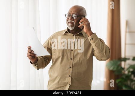 Leitender Mann führte ein Telefongespräch, während er wichtige Dokumente in einem gut beleuchteten Innenbereich hielt Stockfoto