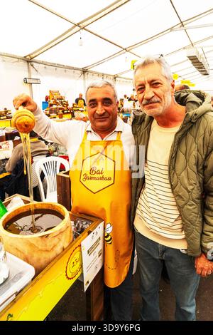 Baku, Aserbaidschan-10. Oktober 2025; Messe, Honig-Supermarkt. Ein Imker, ein Mann und eine Frau stehen am Tisch des Marktes und verkaufen Honig verschiedener Größen in Gläsern. Stockfoto