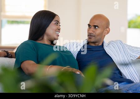 Verschiedene Paare plaudern auf hellem Sofa am Fenster im Wohnzimmer mit grüner Zimmerpflanze Stockfoto