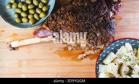 Gebratene Lammkeule auf einem Brett mit Beilagen: Oliven und Maniok-Pommes. Golden, gewürzt, perfekt für ein komplettes und herzhaftes festliches Essen. Stockfoto
