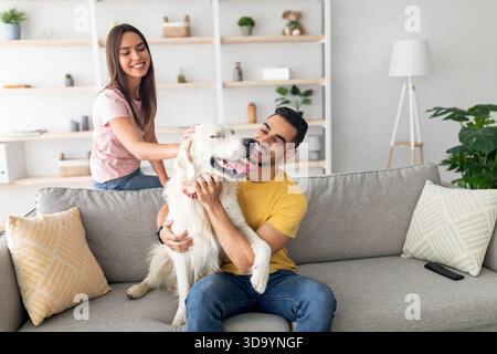Paare genießen spielerische Momente mit ihrem Golden Retriever in einem gemütlichen Wohnzimmer an einem sonnigen Nachmittag Stockfoto