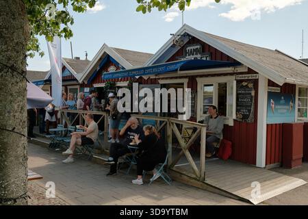 Nynashamn, Stockholmer County, Schweden - 29. Mai 2025: Eine Gruppe von Menschen sitzt vor einem roten Gebäude mit einer Eisdiele. Das Gebäude ha Stockfoto