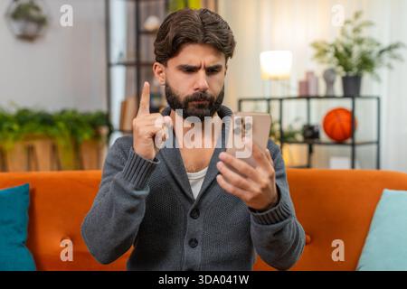 Indischer Mann zu Hause spielt Handy-Casino verliert Wette Seufzer hält Kopf reibt Stirn, keine Geste. Arabianer auf dem Sofa sieht Ergebnis traurig sagt nein mit Hand bestürzt Stimmung nach dem Verlust des Online-Glücksspiels Stockfoto