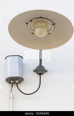 Außenbeleuchtung mit beigefarbenem Schirm und angeschlossenem Schaltkasten an einer weißen Wand Stockfoto