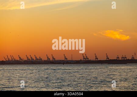 Ein lebhafter Sonnenuntergang zeigt einen industriellen Containerhafen in New York mit Silhouetten von Kränen Stockfoto