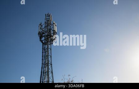 Ein hoher Mobilfunkmast, der vor einem klaren blauen Himmel erfasst wurde und moderne Mobilfunknetzinfrastruktur und Telekommunikationsausrüstung zeigt Stockfoto
