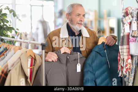 Ein älterer Mann sucht sich eine Daunenjacke in einem Geschäft aus Stockfoto