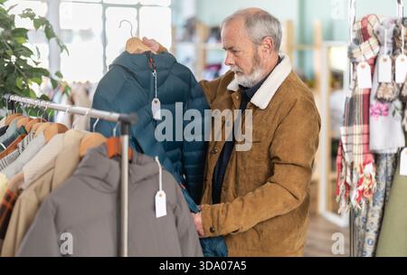 Ein älterer Mann sucht sich eine Daunenjacke in einem Geschäft aus Stockfoto