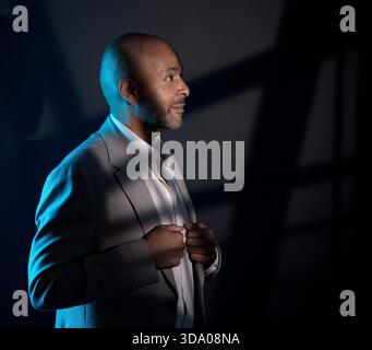 Studio-Porträt eines kahlen afroamerikanischen Mannes, der einen grauen Anzug und ein weißes Hemd mit dramatischer Beleuchtung vor dunklem Hintergrund trägt. Dieses Bild ist sui Stockfoto