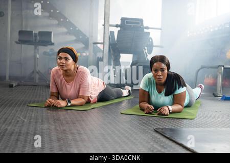 Verschiedene mittelErwachsene weibliche Freunde halten Unterarmplanken auf grünen Matten im Fitnessstudio und tragen Smartwatches Stockfoto