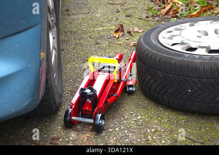 An einem Fahrzeug wird mit Wagenheber und Reserverad gearbeitet, wahrscheinlich aufgrund eines Reifenpangels Stockfoto