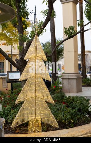Ein hoher beleuchteter Baum steht in einem Einkaufsviertel, umgeben von grünen Pflanzen. Der Baum leuchtet mit Lichtern und sorgt für festlichen Beifall. Stockfoto