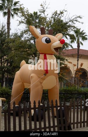 Ein großes aufblasbares Rentier steht auf einem öffentlichen Platz. Er ist mit Seilen festgebunden und hat eine rote Nase. Stockfoto