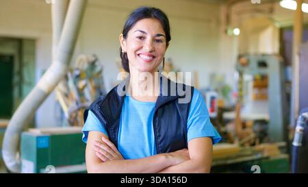 Selbstbewusste Handwerkerin lächelt in der Holzwerkstatt Stockfoto