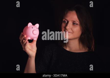 Eine Frau, die eine rosa Sparkasse hält, die finanzielle Ersparnisse und Investitionen repräsentiert. Konzept des Geldmanagementplans und künftiges Wohlstandswachstum. Stockfoto