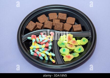 Verschiedene Süßigkeiten und Pralinen auf schwarzem, geteiltem Tablett über pastellfarbenem Hintergrund Stockfoto